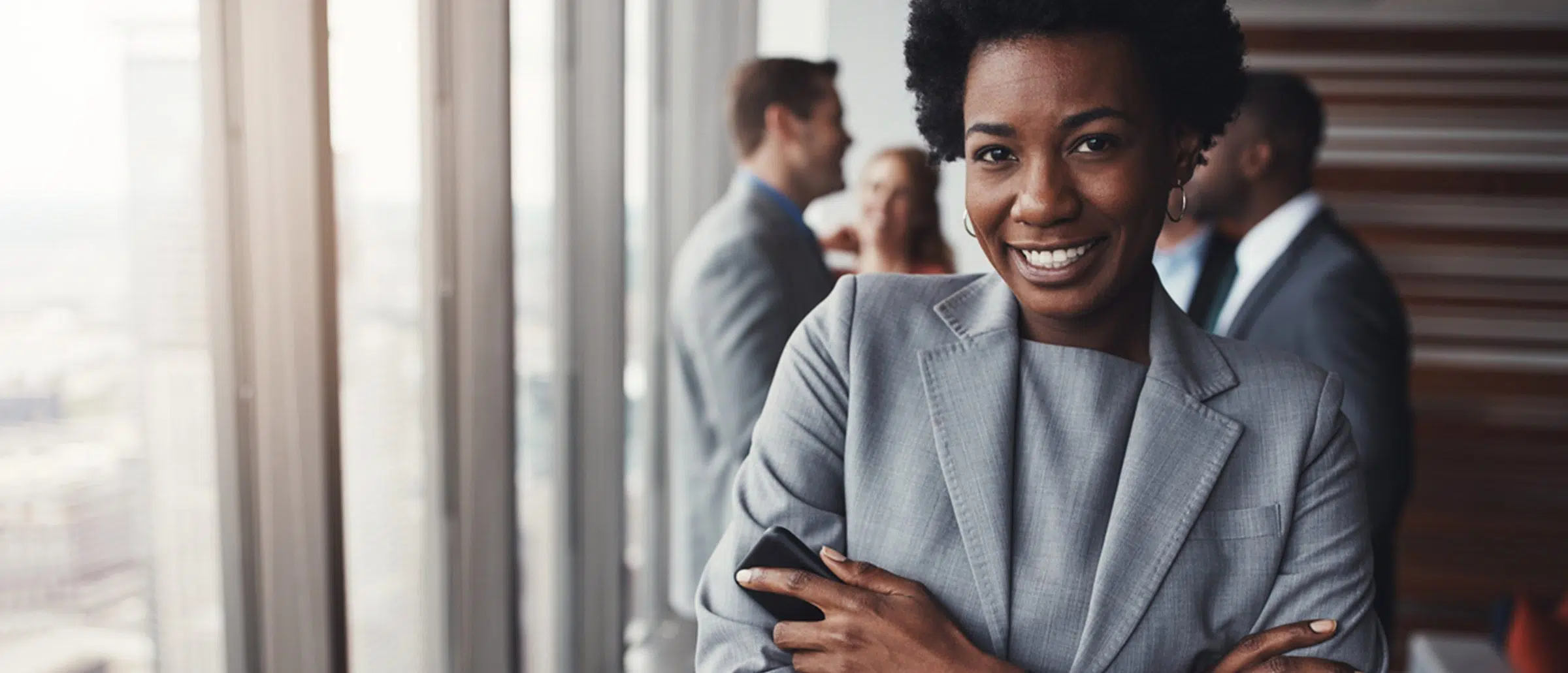 Black businesswoman smiling with her arms folded with business professionals standing behind her