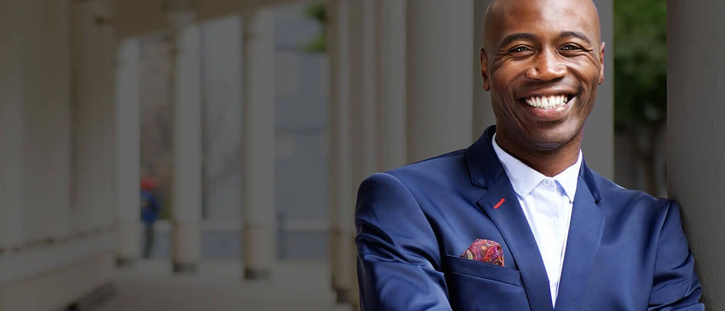 Middle age black businessman wearing a white dress shirt and blue jacket, smiling with folded arms