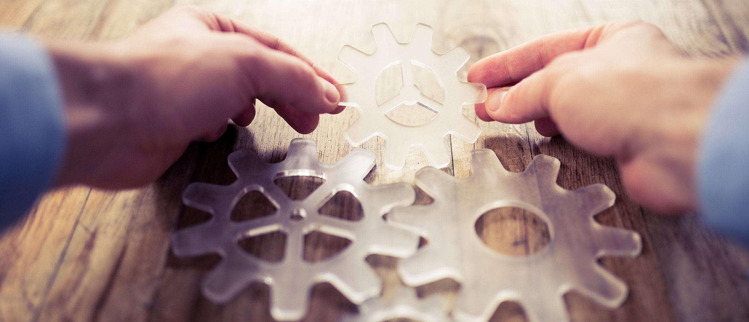 Two hands holding a translucent gear with more gears laid out on a brown table