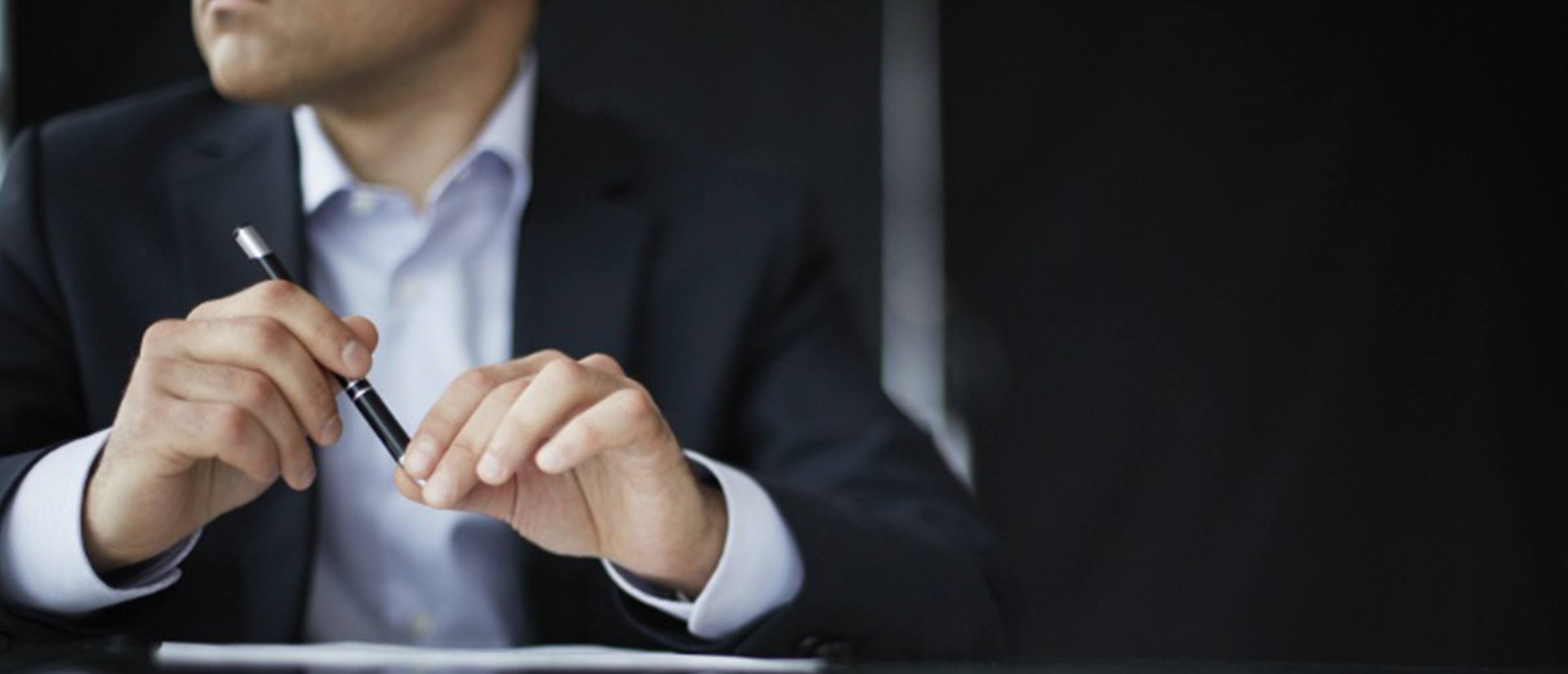 Businessman sitting at a table holding a pen and looking out to his right