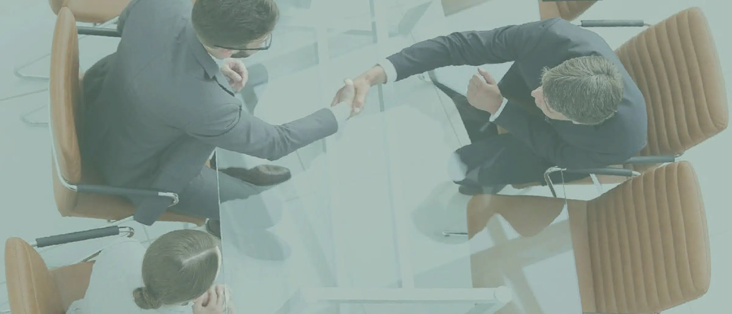 Two businessmen shaking hands at a table with a businesswoman sitting near them