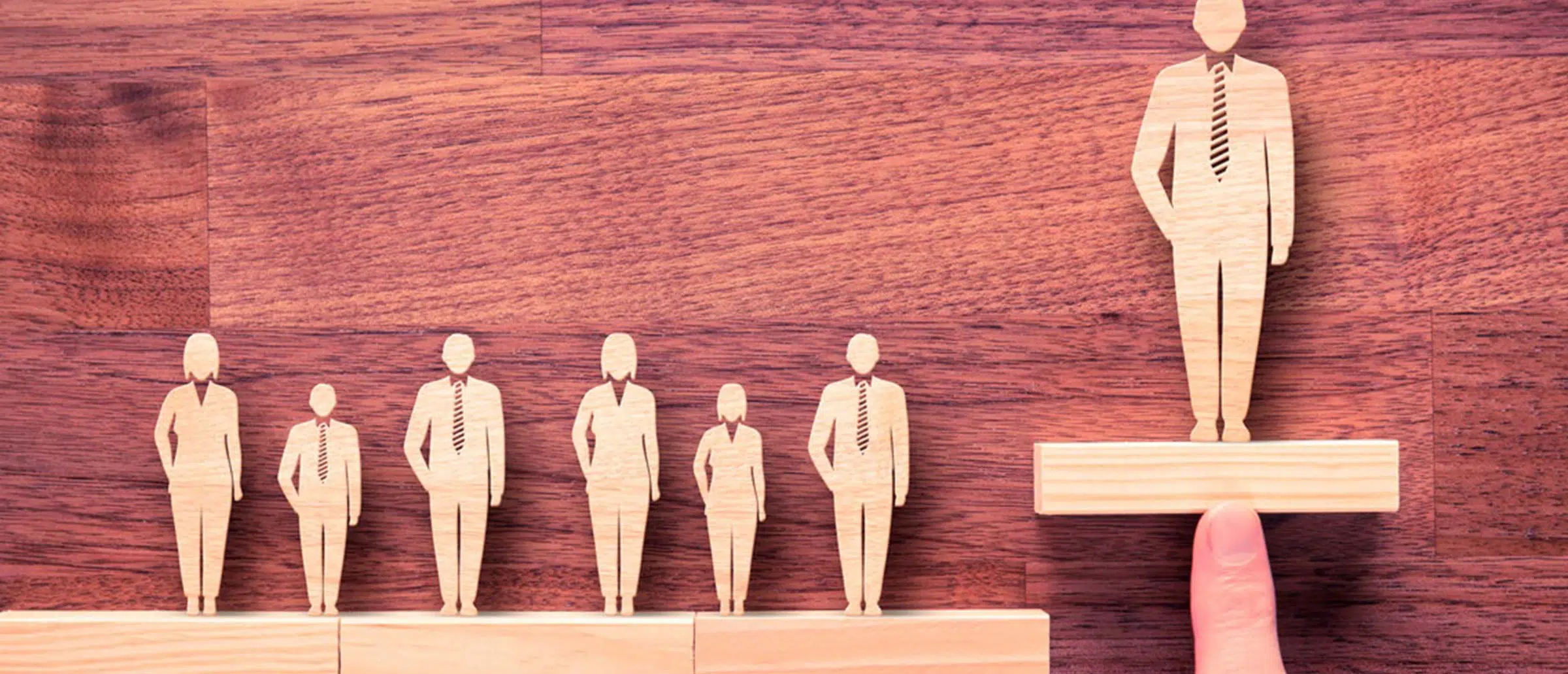 A row of wooden human figures with a larger wooden figurine placed higher than the others